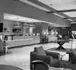 Hotel lobby with armchairs and a long, wood front desk divided by a wall.