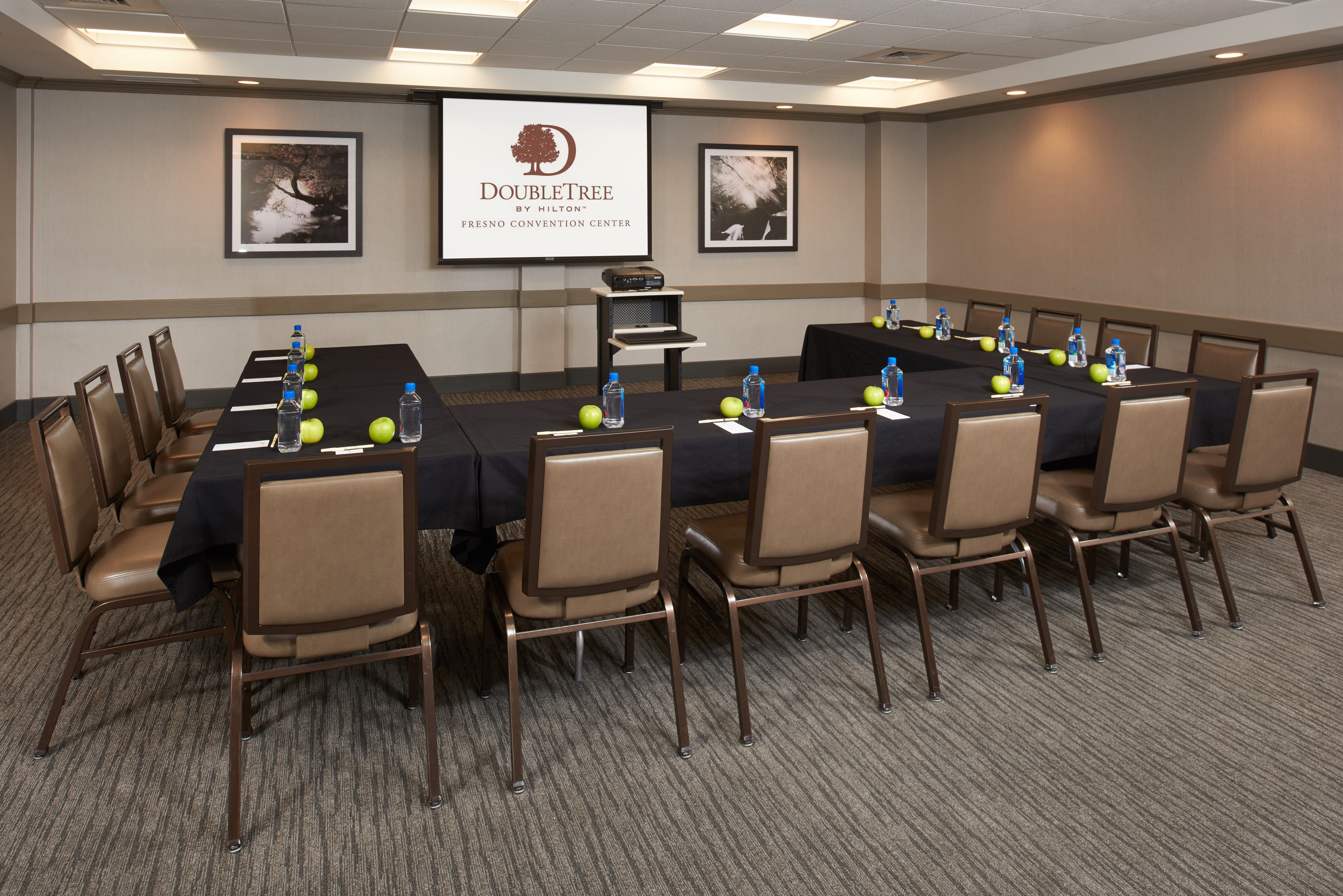 Sierra Meeting Room With U-Shaped Table and 14 Chairs Facing Audio/Visual Equipment Table, Wall Art, and Presentation Screen