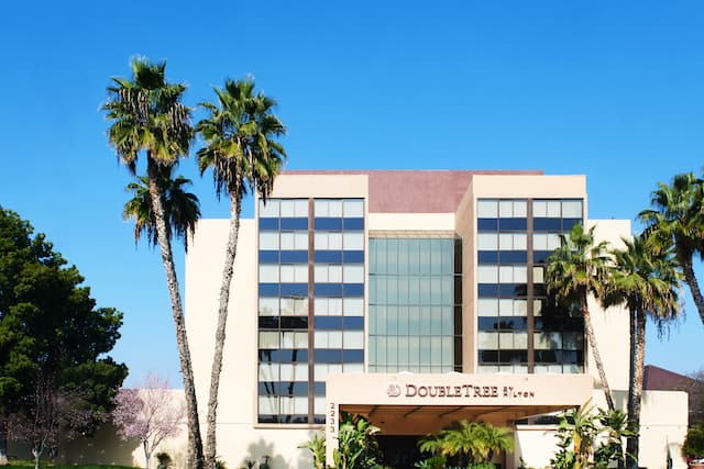 Daytime View of Hotel Exterior, Signage, Flagpole, Landscaping, Porte Cochere, and Guest Cars on Parking Lot