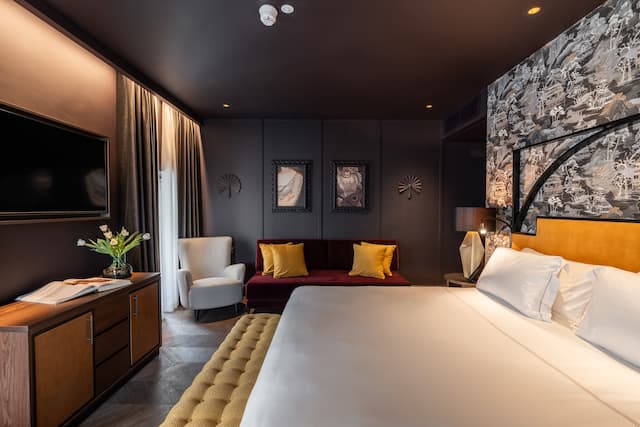 Chambre avec très grand lit, canapé et fauteuil en velours et téléviseur