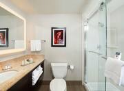 Large Vanity Mirror, Sink, Fresh Towels, Amenities, Toiletries, Wall Art Above Toilet, and Shower With Glass Doors