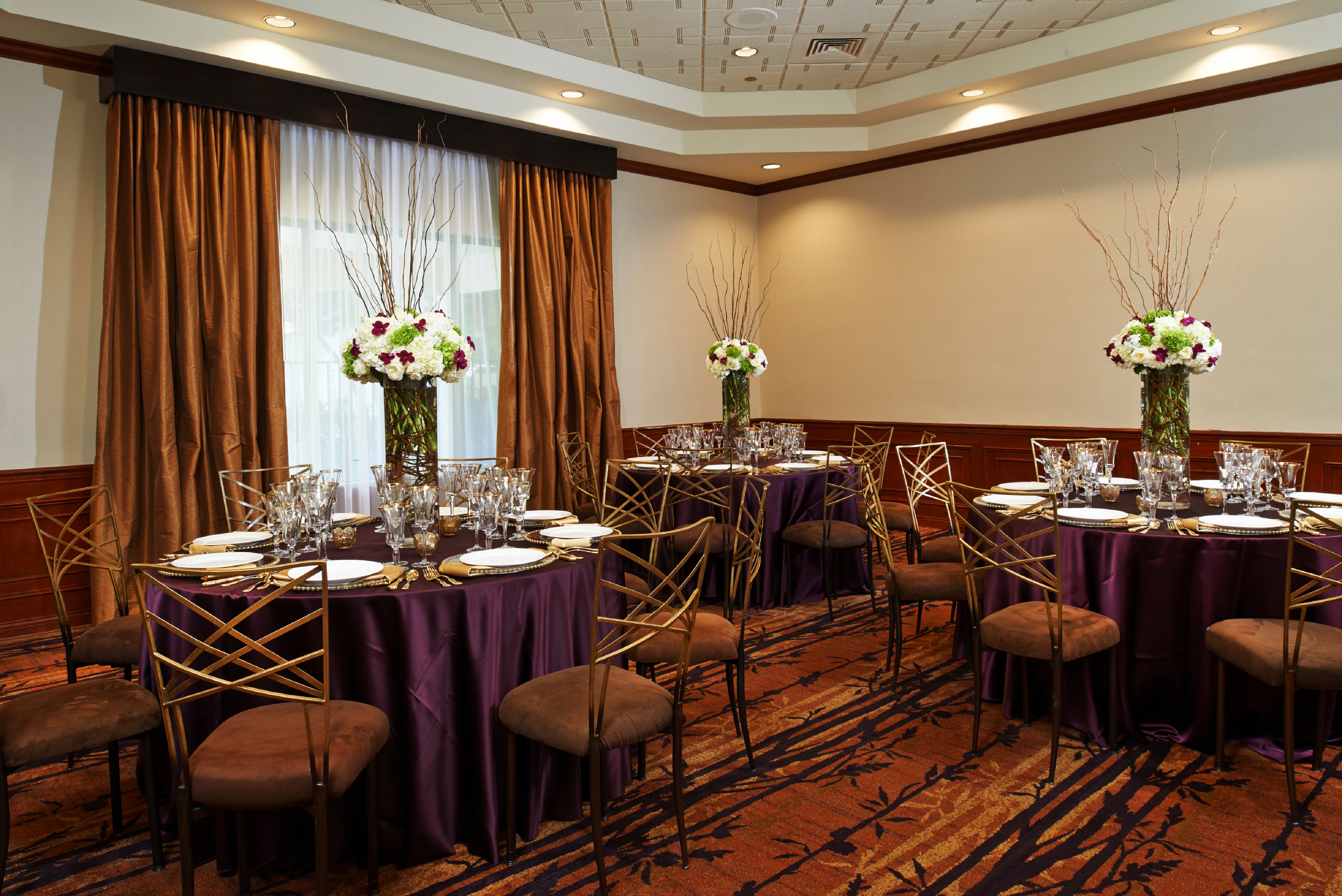 Round Dining Tables With Place Settings and Flowers on Purple Linens in Meeting Room Decorated for Wedding 