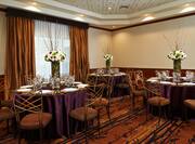 Round Dining Tables With Place Settings and Flowers on Purple Linens in Meeting Room Decorated for Wedding 