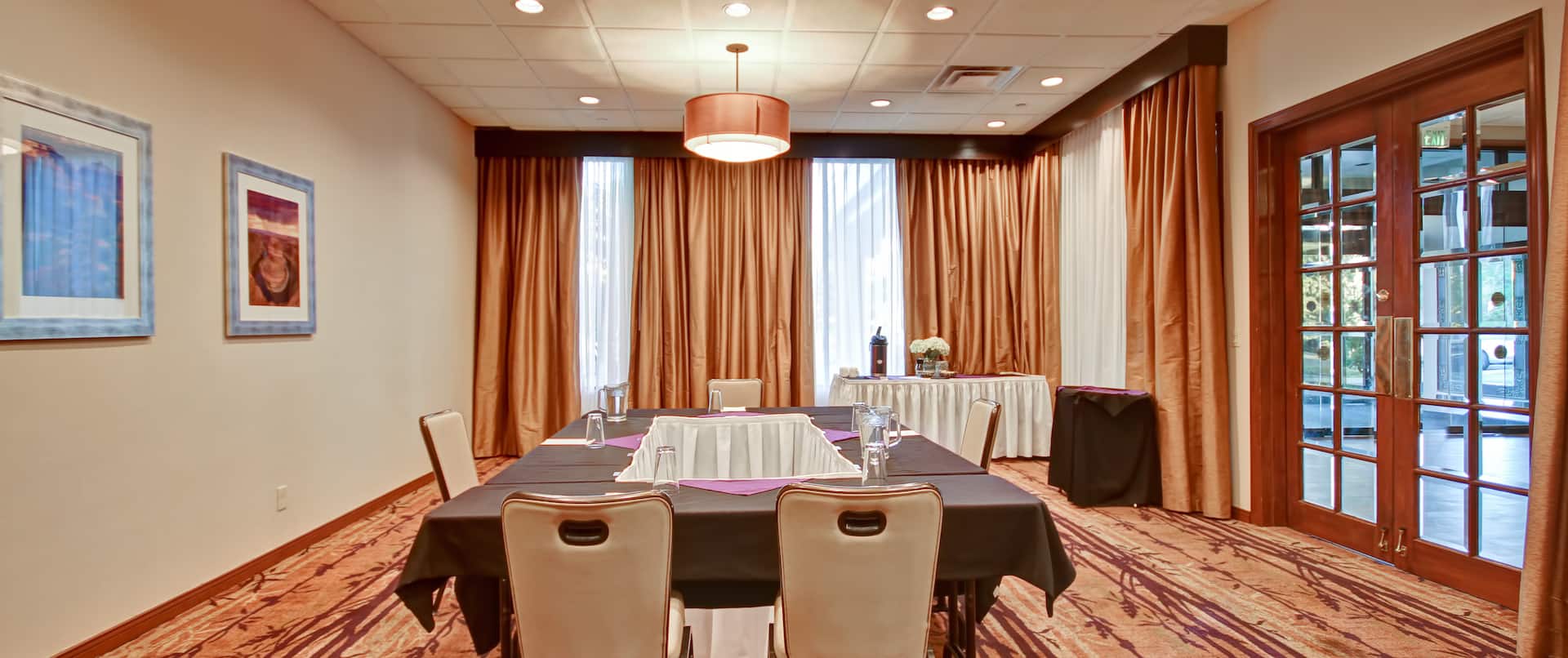 Wall Art, Table With Closed Drapes, Glass Entry Door, Drinking Glasses, and Napkins on Table With Black Linens, Refreshment Table in Meeting Room  