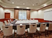 Meeting Room With Notepads and Black Linens on U-Shaped Table, Chairs, Entry Door, Window With Sheer Drapes, and Presentation Screen