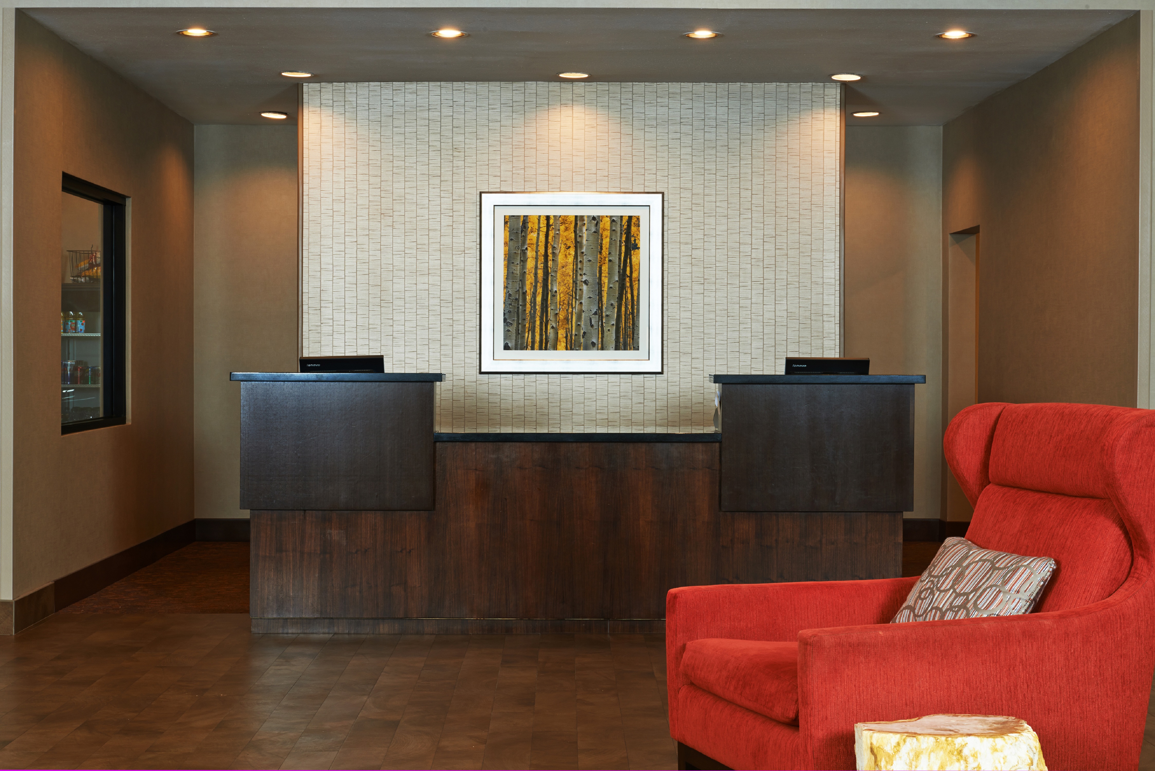 Reception Area With Red Armchair in Sitting Area and Wall Art Behind Front Desk With Two Computers