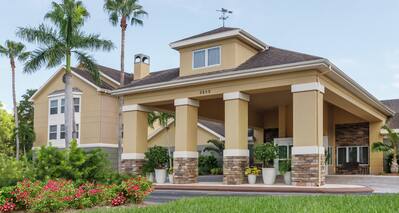 Welcoming Homewood Suites hotel featuring porte cochere, beautiful flowers, and tall palm trees.