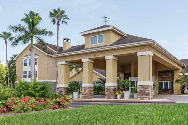 Welcoming Homewood Suites hotel featuring porte cochere, beautiful flowers, and tall palm trees.