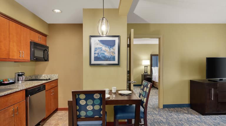 Spacious living area in suite featuring fully equipped kitchen, dining table, and TV. 