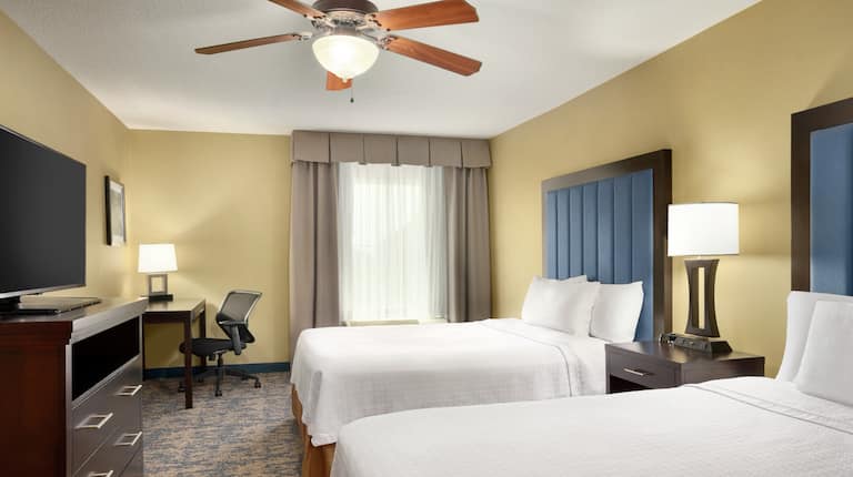 Private bedroom in suite featuring a TV, work desk, and two comfortable queen beds.