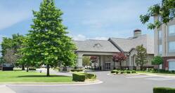 Welcoming Homewood Suite Hotel featuring lush landscaping, porte cochere, and bright blue sky.