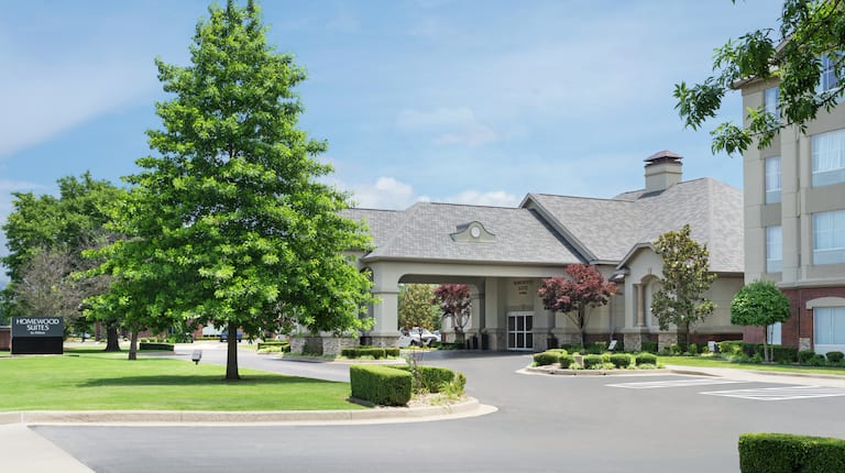 Welcoming Homewood Suite Hotel featuring lush landscaping, porte cochere, and bright blue sky.