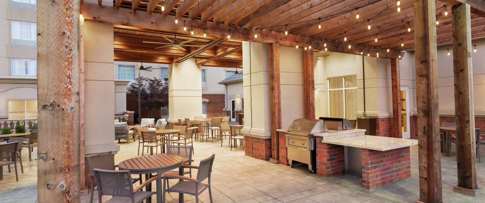 Beautiful outdoor pergola area for guests to relax featuring ample seating, bbq grills, and string lights.