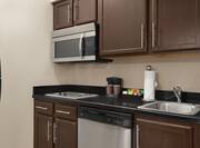 Functional kitchen in suite featuring fridge, dishwasher, microwave, coffee maker, and cooktop stove.