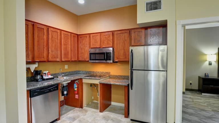 A Kitchen in a Hotel Suite with Mobility Accessible Counters, a Fridge, Dishwasher and Microwave
