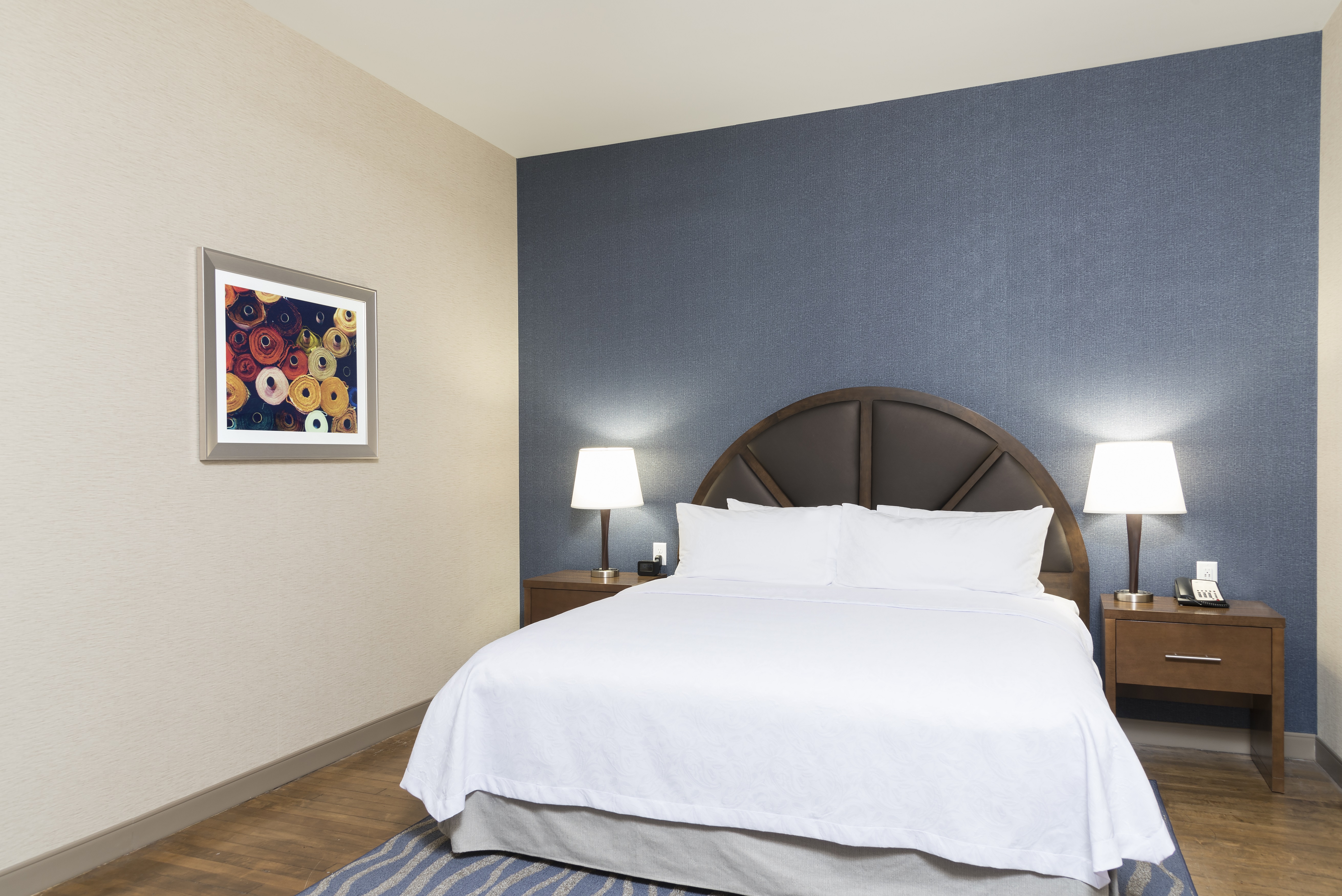 Wall Art and Queen Bed Between Two Illuminated Lamps on Bedside Tables in Suite