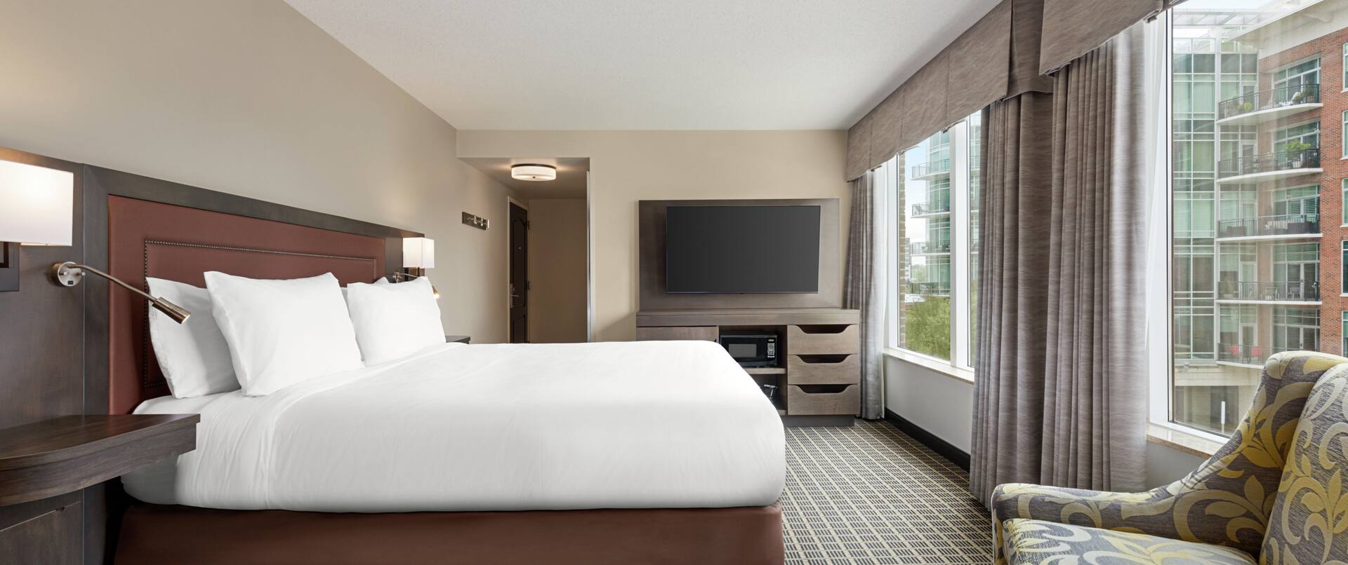Spacious guestroom featuring comfortable king bed, TV, and beautiful city view.