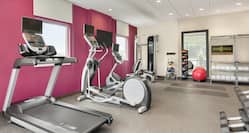 Spacious fitness center featuring cardio machines, free weights, yoga mats, mirror, and complimentary towels.