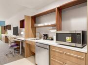 Fully equipped accessible kitchen in studio suite next to living area with work desk and TV.