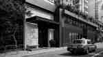 Exterior of hotel with a sidewalk, and a taxi passing by.