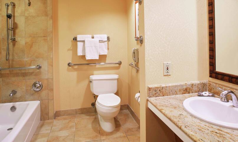 Chambre pour personnes à mobilité réduite dans la tour Tapa avec toilettes, miroir, comptoir lavabo, baignoire et douche, transition précédente