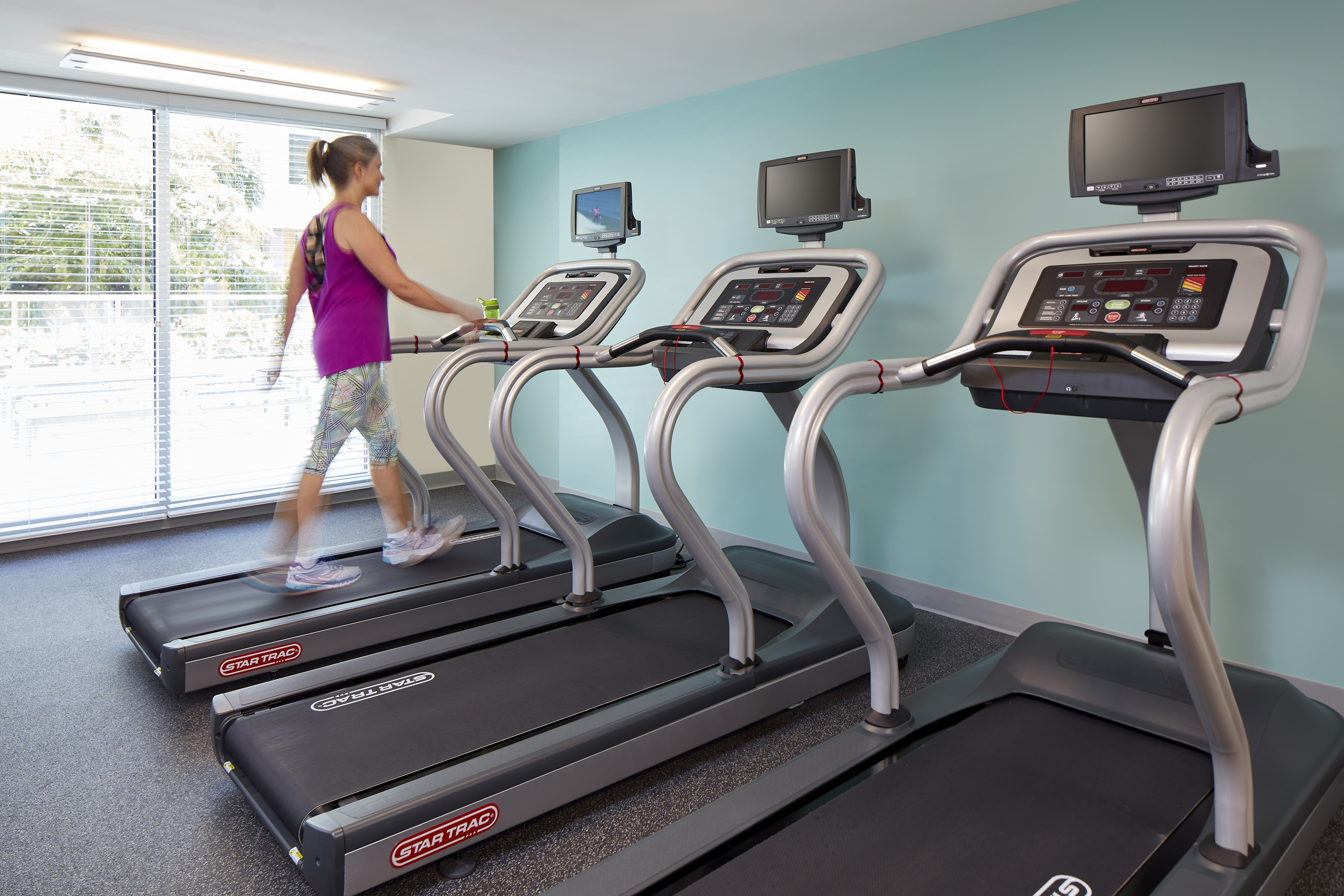 Woman on One of Three Fitness Center Treadmill by Large Windows