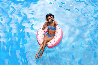 Black woman in blue bikini swimming on inflatable ring at pool during tropical vacation.