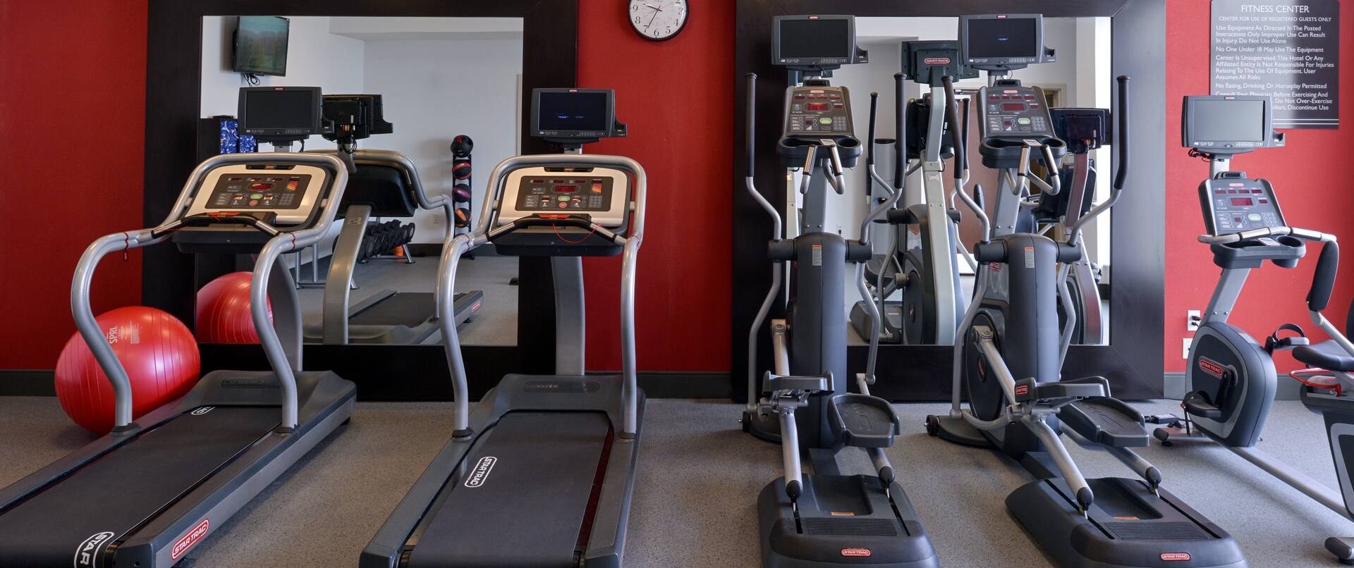 Fitness Center With TV, Red Exercise Ball and Cardio Equipment Facing Large Wall Mirrors, 
