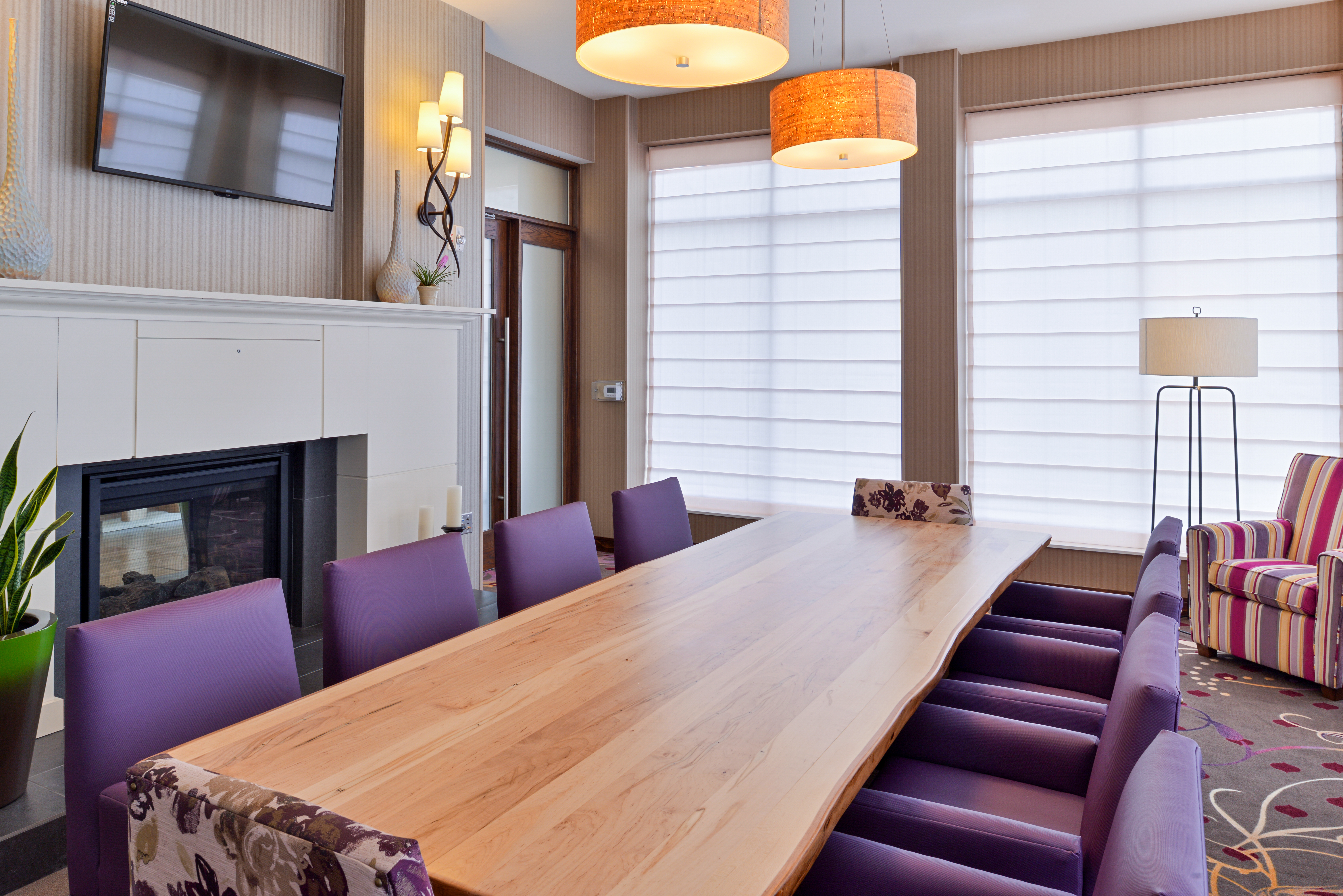 Conference Room with TV Above Fireplace, Large Windows, Long Table, Ten Purple Chairs and Armchair in Corner  by Window