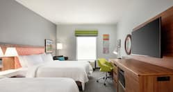 Spacious guest room featuring comfortable two queen beds, TV, and work desk.