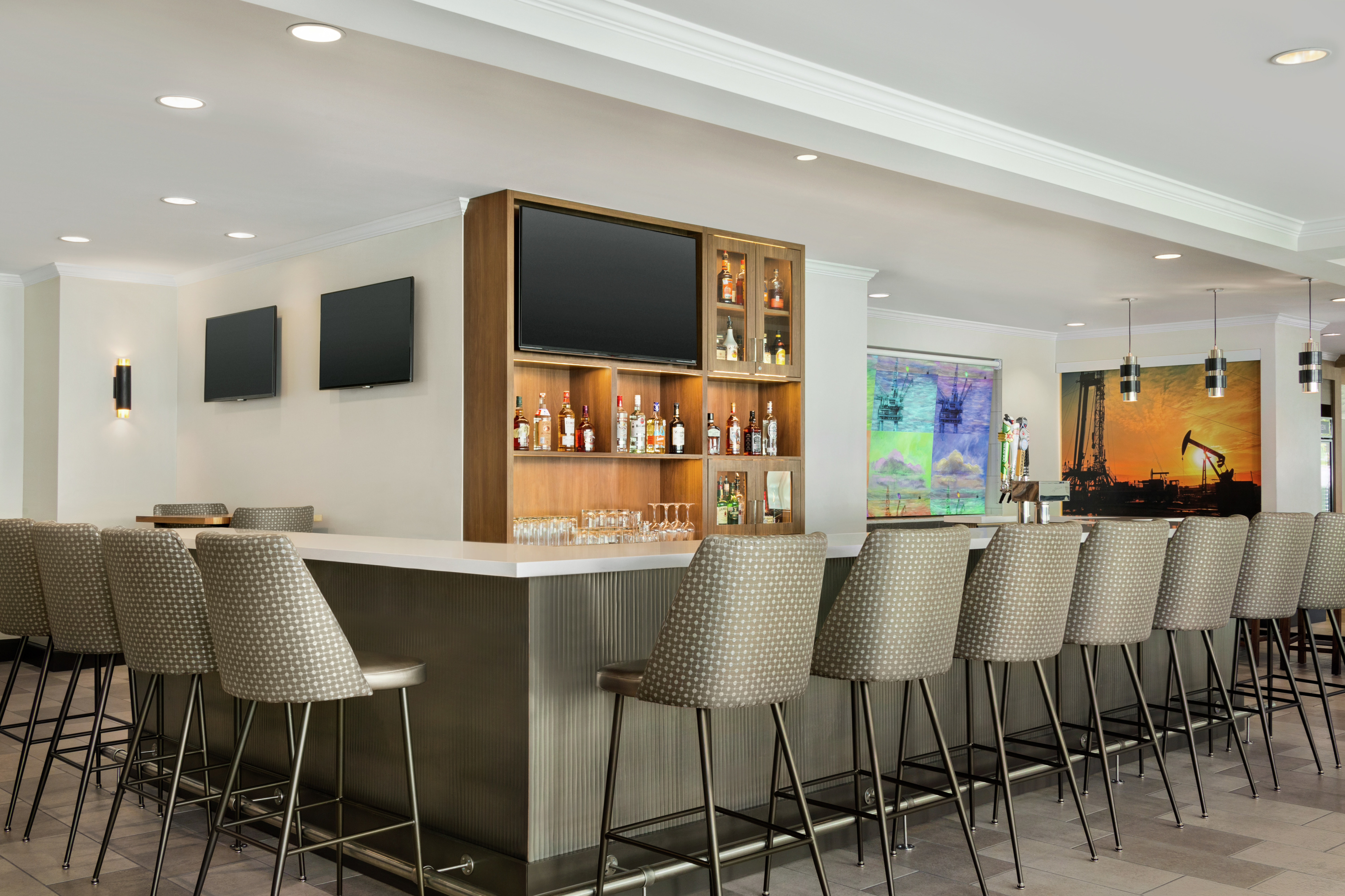 Spacious hotel bar area featuring ample seating, TVs, and local artwork.