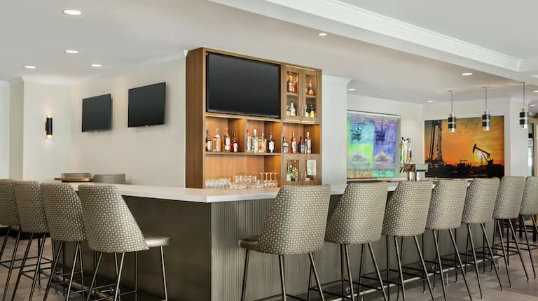 Spacious hotel bar area featuring ample seating, TVs, and local artwork.