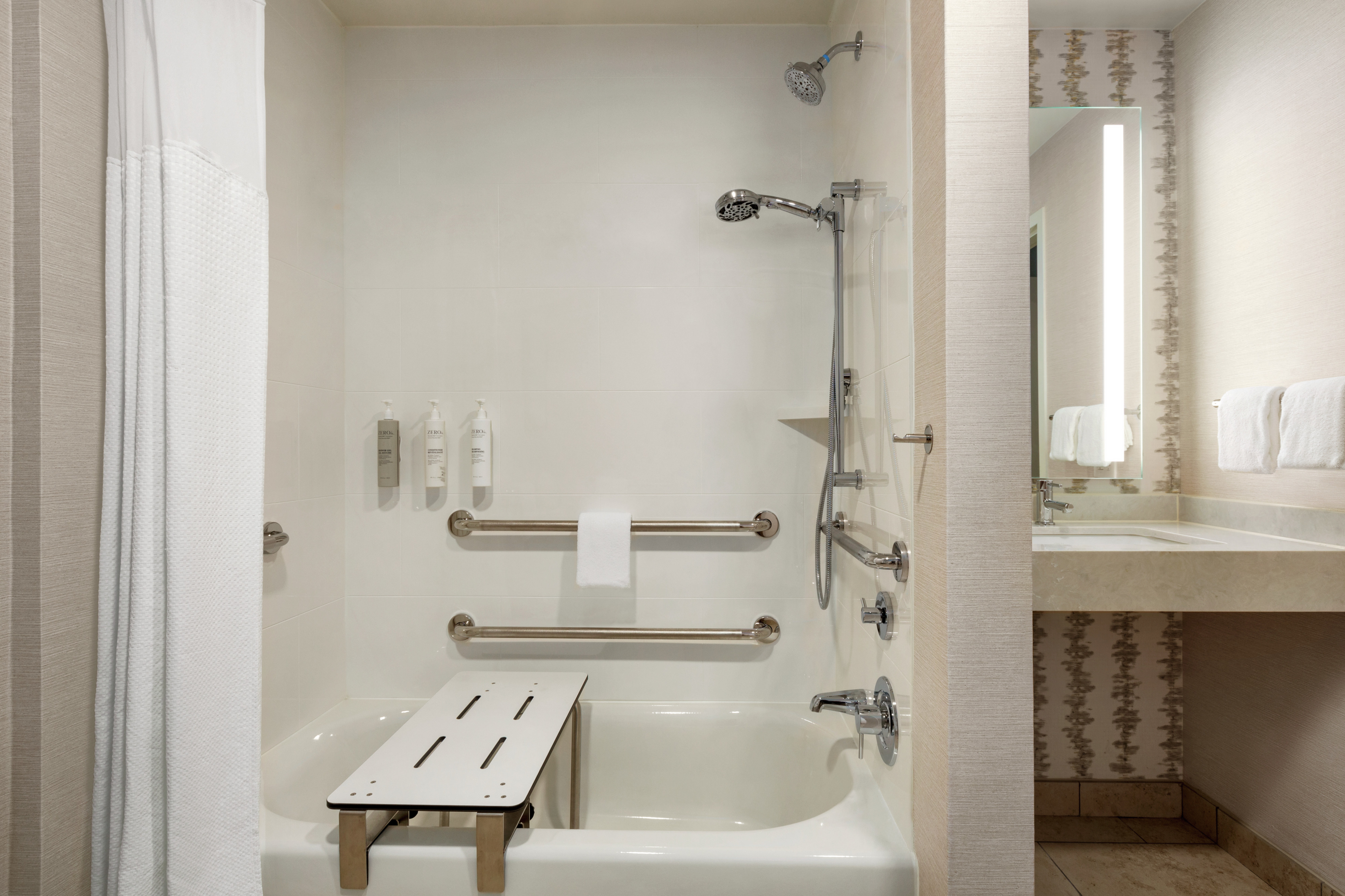 Spacious accessible bathroom featuring tub with seat and grab bars for guest safety.