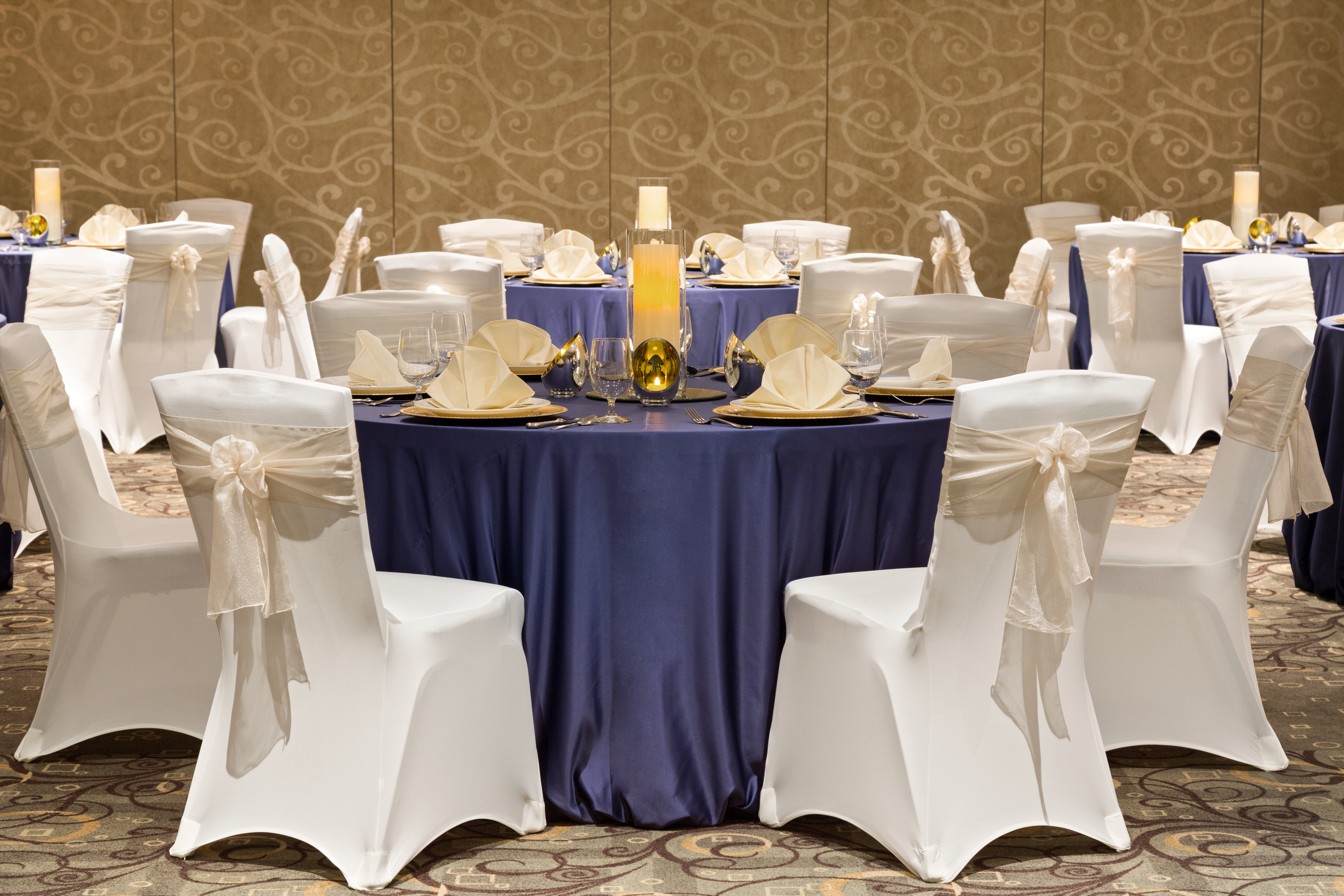 Ballroom Set Up With Place Settings on Round Tables With Purple Tablecloths and Chairs With White Covers