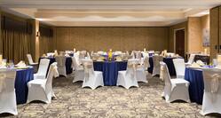 Wide View of Round Tables With Purple Tablecloths and Chairs With White Covers in Ballroom Set Up