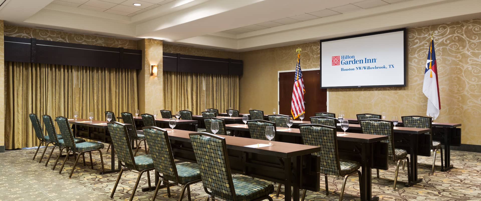 Classroom Style Meeting Room With Tables and Chairs Facing Presentation Screen  Between American and Texan Flags