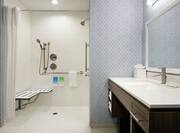 Spacious accessible bathroom featuring roll in shower with seat, vanity, and mirror.