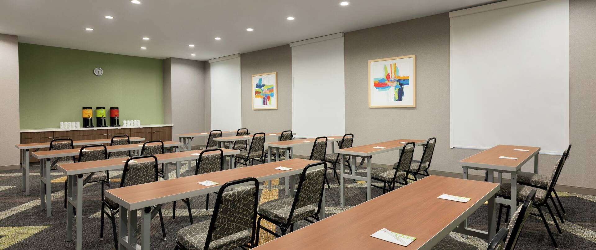 Spacious meeting room with classroom style tables, chairs, notepads, pens, and refreshment station.