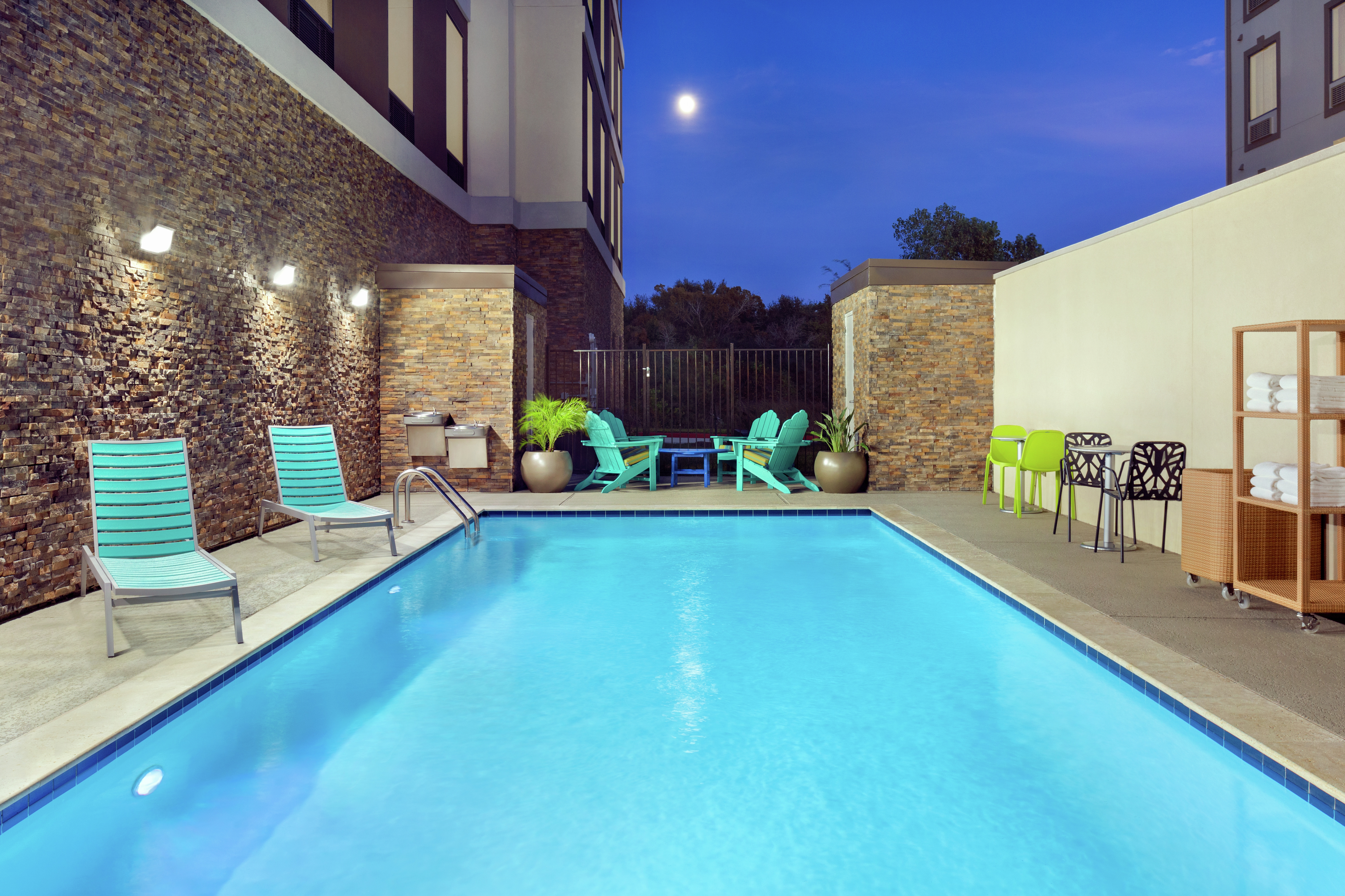 Outdoor pool at night with privacy walls,  lounge chairs, and complimentary towels.