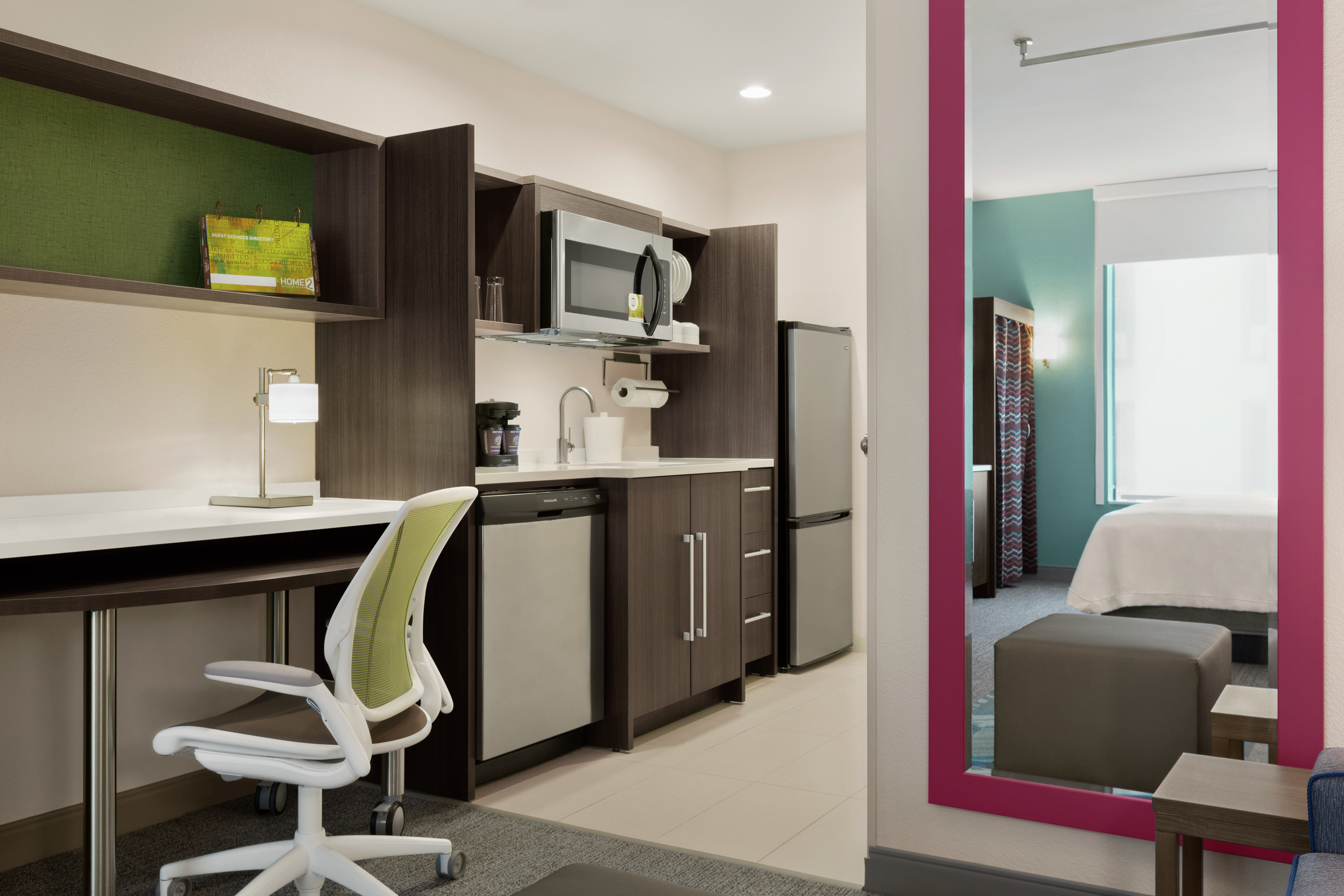 Spacious studio suite with fully equipped kitchen, work desk with ergonomic chair, and full length mirror on wall.