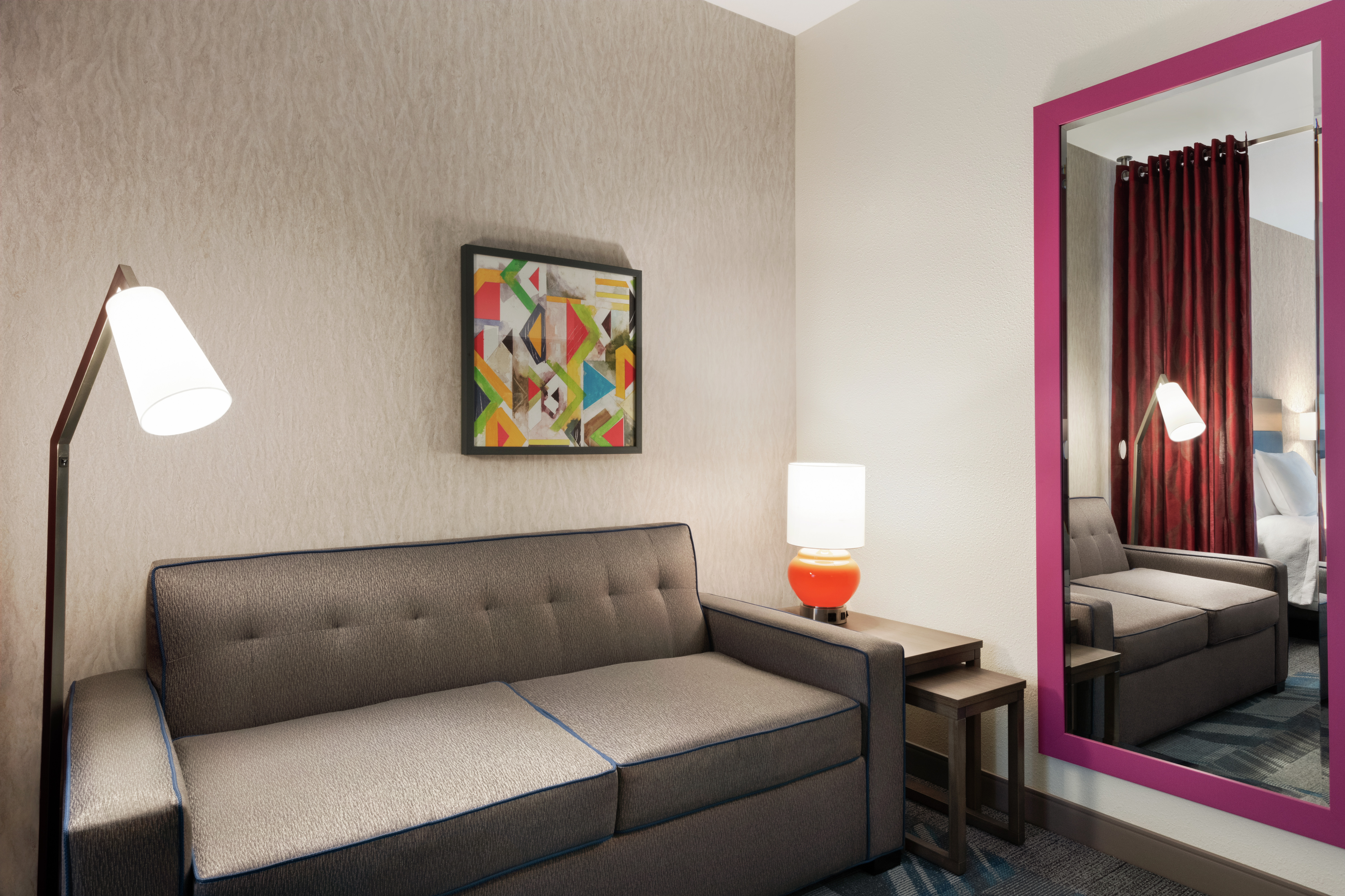 Studio suite lounge area with sofa, fully length mirror, and geometric framed art on wall.