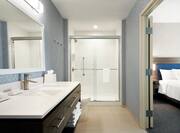 Bright en-suite guest bathroom featuring large vanity, mirror, and walk in shower.
