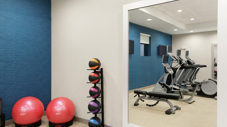 Spacious fitness center featuring cardio machines, medicines balls, and full length mirror.
