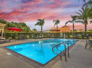 Outdoor gated pool with lounges and surrounded by palm trees at sunset