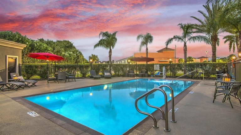 Outdoor gated pool with lounges and surrounded by palm trees at sunset