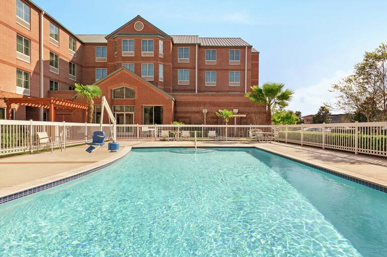 Large outdoor swimming pool featuring accessible chair lift, patio furniture, and surrounding gate for safety.