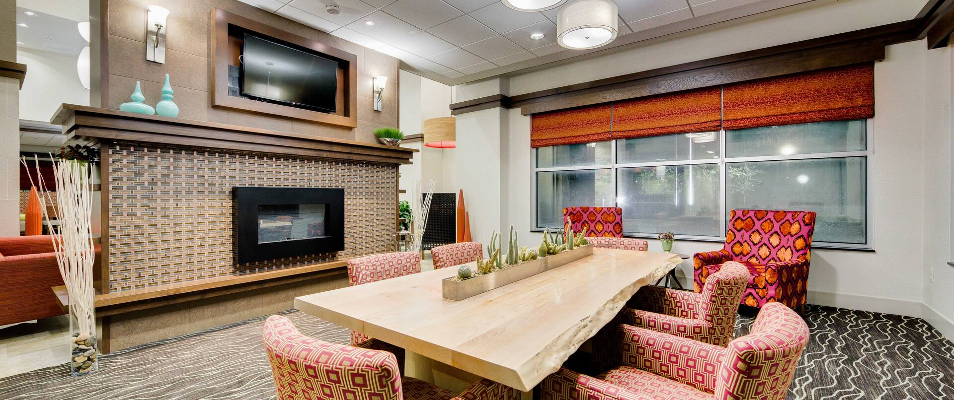 TV Above Fireplace, Table With Seating for Six, and Two Arm Chairs by Windows in Library Lounge Area 