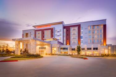 Illuminated Hotel Exterior, Signage, Circle Driveway, Landscaping, and Guest Cars on Parking Lot at Dusk