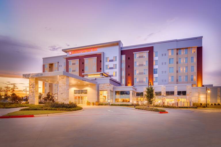Illuminated Hotel Exterior, Signage, Circle Driveway, Landscaping, and Guest Cars on Parking Lot at Dusk