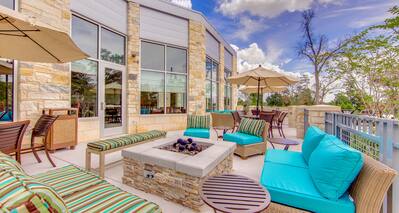 Daytime View of Outdoor Patio and Fire Pit Surrounded by Soft Seating, Tables, and Sun Umbrellas
